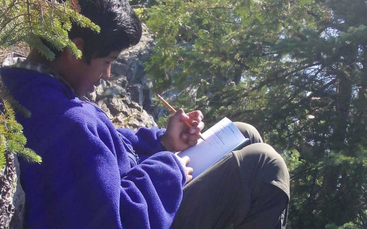 A person rests agains a rock while journaling. 
